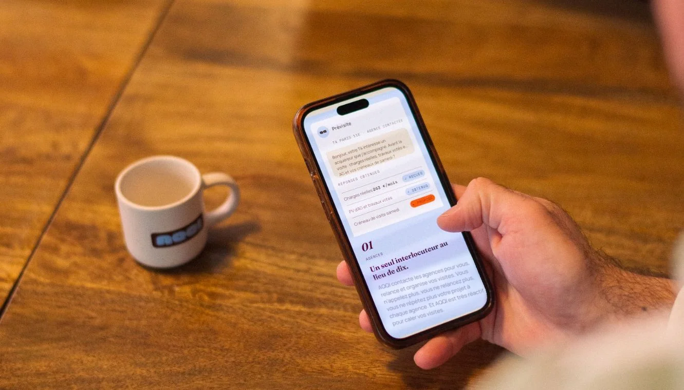Un téléphone affichant la prévisite AQQI, posé à côté d’une tasse AQQI sur une table en bois.